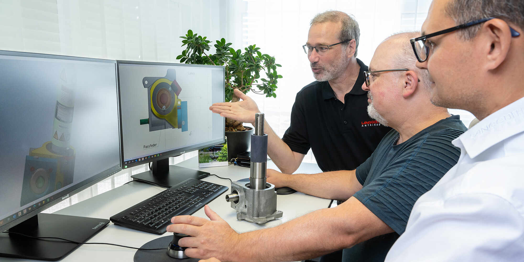 Drei Männer reden über eine 3D Darstellung eines Getriebes auf einem Monitor